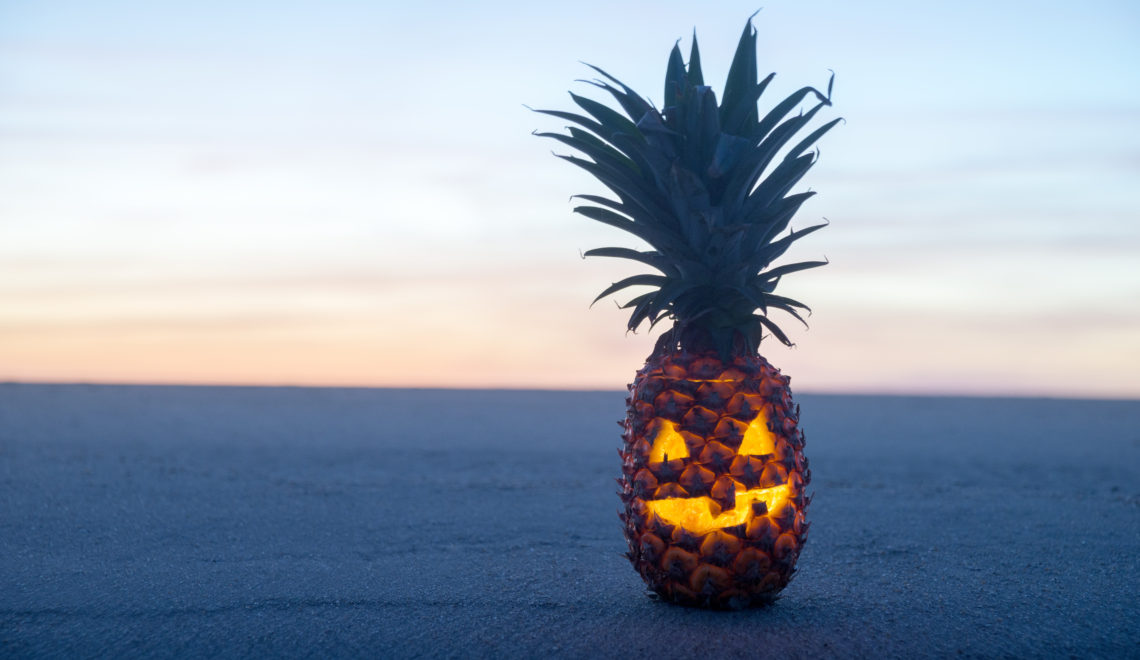 Pineapple carved like jack-o-lantern on the beach at sunset